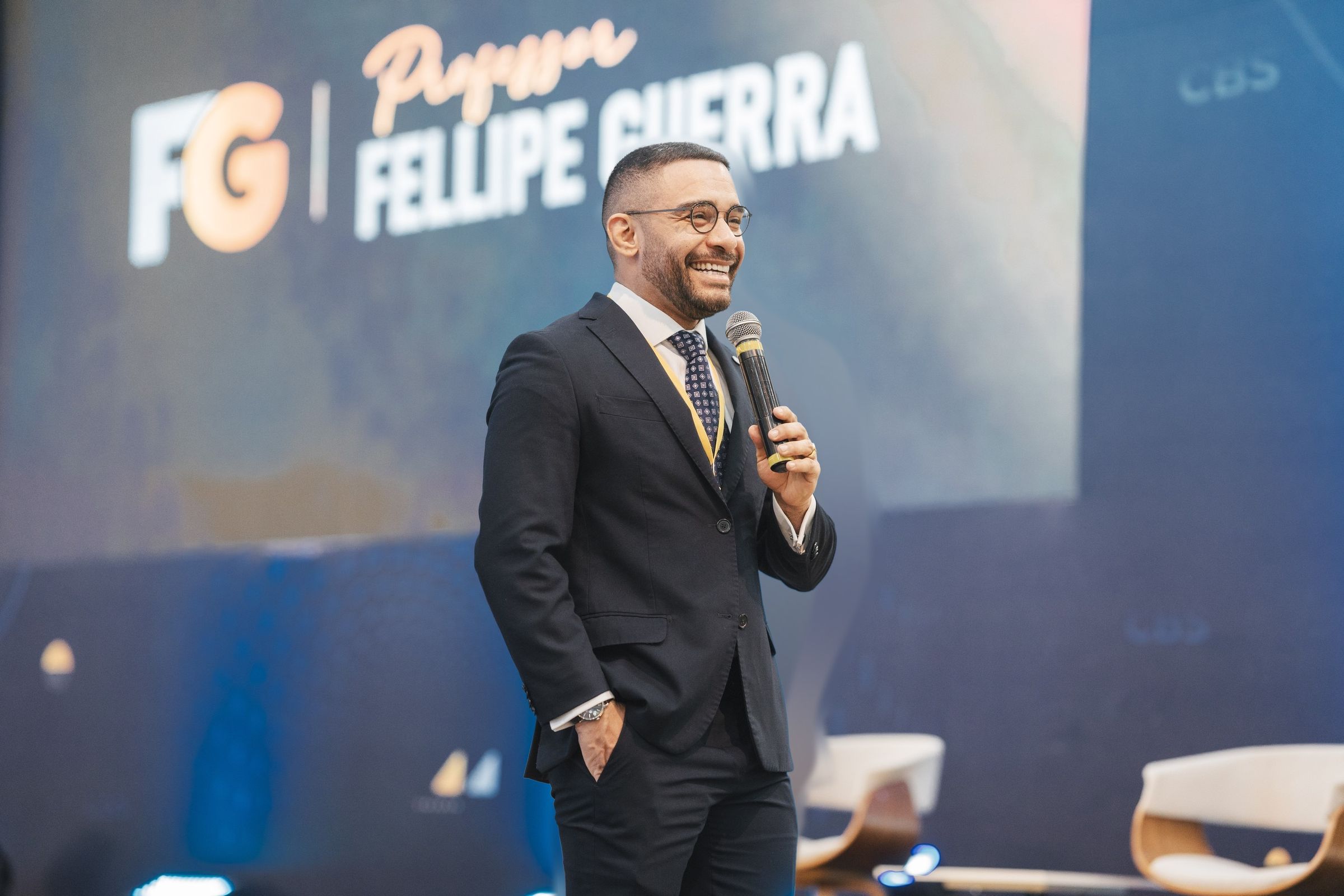 Prof. Fellipe Guerra no palco, com o nome dele no telão ao fundo